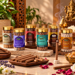 Six clear jars of dhoop sticks with gold lids, arranged on a stone surface with a lit stick and rose petals.