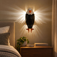 A geometric black and white eagle wall light with bright light radiating from its sides, mounted above a nightstand.