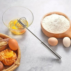 A compact stainless steel egg whisk with its spring mechanism visible.