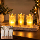 Three clear plastic LED candles with warm yellow glow on a textured rectangular tray, surrounded by dim ambient light and a