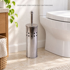 A tall, cylindrical stainless steel toilet brush holder with square cutouts, positioned on a tiled floor beside a white