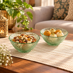 Two green glass bowls filled with nuts and sweets on a patterned table runner, with a golden lantern nearby.