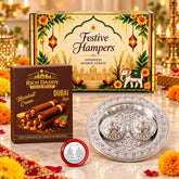 A festive gift hamper featuring a decorative box, a box of hazelnut cream cigar rolls, a silver kumkum dish, and a red coin