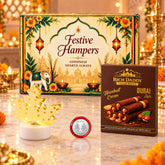 A festive gift hamper with a decorative box, a gold maple leaf lamp, and a box of hazelnut wafer rolls.