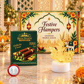 A festive hamper box, pistachio cream cigar rolls, a gold maple leaf lamp, and a silver coin on a marble surface with lit