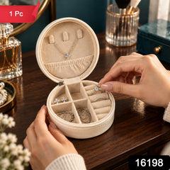 A person's hands placing a silver ring with a clear stone into a cream-colored round jewellery box with a red "1 Pc" label.