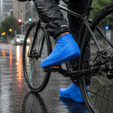 A person on a bicycle wears blue waterproof shoe covers on a wet city street