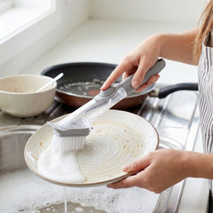 Hand using soap dispensing dish scrub brush to clean a pan