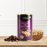 A purple and gold tin of chocolate-coated nuts sits on a wooden surface with loose cashews and chocolate pieces.