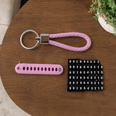 A pink braided wrist loop keychain, a pink number tag, and a sheet of number stickers on a wooden table.