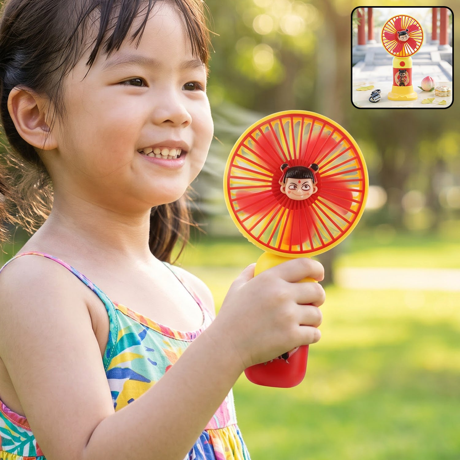 A young girl smiling and holding a red and yellow mini fan with a cartoon character face in the center.