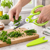 Hands chop fresh green parsley with lime green and white kitchen scissors on a wooden board.