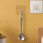 A silver spoon hanging from a transparent self-adhesive hook on a yellow wall, with a close-up inset.