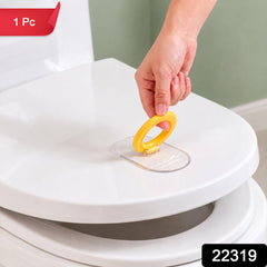 A hand lifts a white toilet seat with a yellow ring and clear base, showing the product in use.