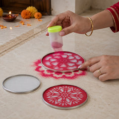 A person's hands use a stencil and pink powder to create a rangoli design on a light floor, with a lit diya nearby.