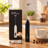 Black handheld milk frother, its packaging, and a white USB cable on a wooden counter with coffee.