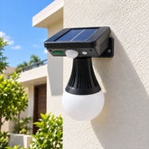 Black solar motion sensor light with a white globe bulb attached to a cream wall outdoors.