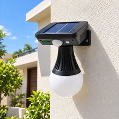 Black solar motion sensor light with a white globe bulb attached to a cream wall outdoors.