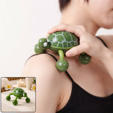 A person's hand guides a green turtle-shaped massager with four rolling feet across their shoulder, providing relief.