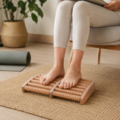 A person's bare feet on a wooden foot massager on a woven mat, with a rolled yoga mat in the background.
