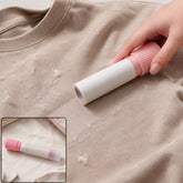 A hand uses a pink and white lint roller on a beige t-shirt covered in lint, with a smaller inset showing the roller.