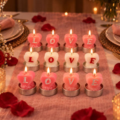 Twelve lit heart-shaped tealight candles in pink and white, arranged on a pink table runner with rose petals.