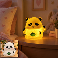 A glowing yellow panda night light sits on a wooden bedside table with a pink pillow and bunny plush in the background.