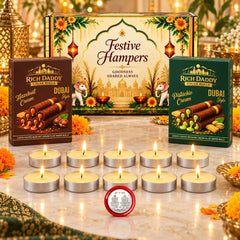 A festive gift hamper box, two boxes of wafer rolls, ten lit tea light candles, and a silver coin on a marble surface.