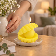 A person's hands adjust a vase of white flowers next to a lit yellow shell candle on a small ceramic plate.