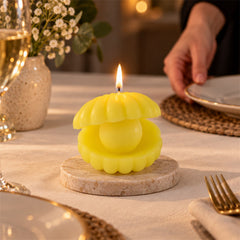 A bright yellow shell candle on a round marble coaster illuminates a dining table setting with a person in the background.