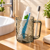 Dark grey textured plastic mug holding a white toothpaste tube and a toothbrush on a wooden bathroom counter.