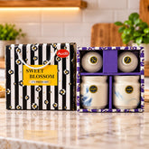 A black and white striped gift box with a yellow label and two ceramic jars in a purple box.