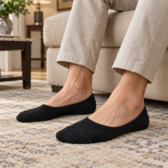 A person's feet wearing black low-cut socks, sitting on a textured rug in a living room setting.