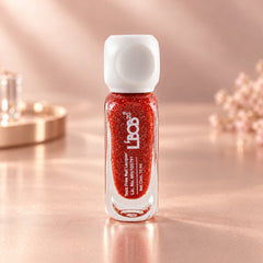 A small, clear glass bottle of red glitter nail polish with a white cap sits on a pink surface.
