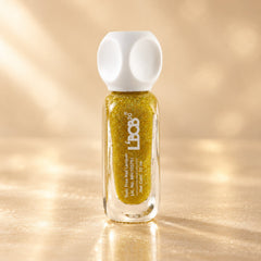 A bottle of gold glitter nail polish with a white cap stands on a reflective gold surface.