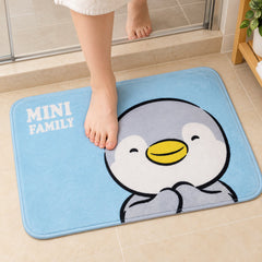 A person's bare feet are shown on a blue bath mat with a smiling penguin graphic, located in a tiled bathroom.