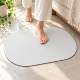 Bare feet stepping onto an oval white mat on a light tiled floor next to a sofa.