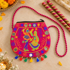 A pink sling bag with embroidered dancing figures, mirrors, and colorful tassels rests on a wooden surface.