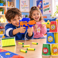 A boy aims an orange and blue toy gun, shooting a yellow foam bullet at a stack of numbered cups, with a girl smiling beside