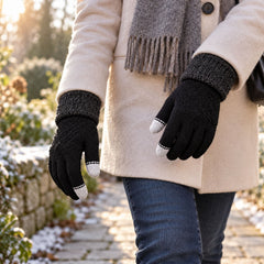 Person in a cream coat and gray scarf, wearing black knit gloves with gray cuffs, walking on a snow-dusted path.