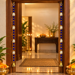 A pair of blue and white decorative hangings with golden bells frame a doorway, with brass pots containing marigolds on the