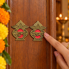A hand points to a golden Shubh Labh sticker set on a wooden door, surrounded by orange flowers.