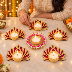 A person's hand lighting a candle in one of the six golden and magenta lotus-shaped tealight holders on a wooden table.