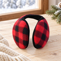 Red and black plaid ear warmers rest on a wooden surface beside a white knitted scarf and snowy window.