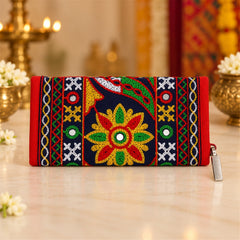 The embroidered clutch wallet rests on a light-colored surface, surrounded by small white flowers and blurred golden decor.