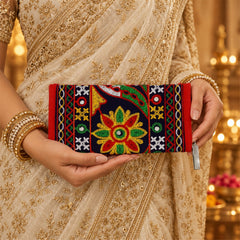 A person in a golden saree holds a dark blue and red embroidered clutch with a colorful floral design.