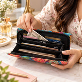 A woman's hands opening a colorful mandala print wallet, revealing cash and cards inside. It has a black interior.