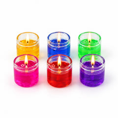 Six lit gel candles in glass jars, in yellow, blue, green, pink, red, and purple, arranged on a white background.