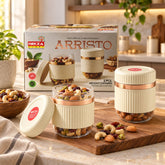 Two clear and cream ribbed containers with rose gold bands, one open, filled with nuts and dried fruit on a wooden board.
