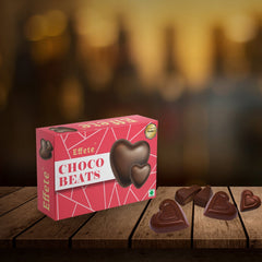 Pink box of heart-shaped chocolates with candies scattered on a rustic wooden surface, blurred warm lights.